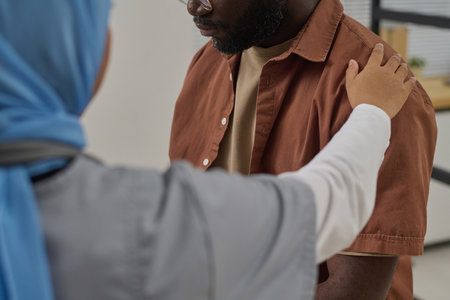Unrecognizable doctor putting hand on shoulder of her black male patient as sign of moral supportの写真素材