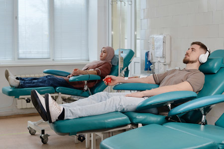 Caucasian man and muslim woman relaxing side by side in clinic during blood donationの写真素材