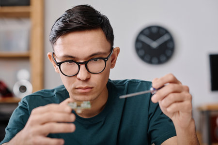 Serious caucasian technician in glasses attentively examining mainboard and using screwdriver