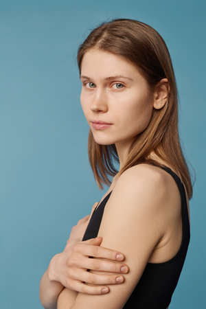 Vertical medium close-up studio portrait of young Caucasian woman standing with arms crossed looking...