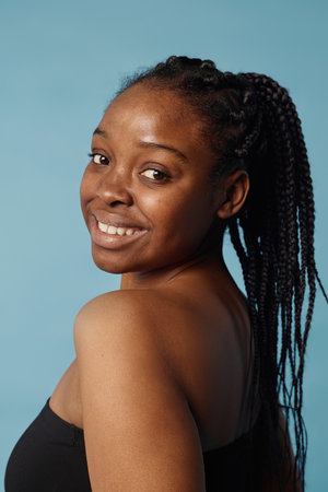 Vertical medium closeup of self-confident African American girl with braided hair posing for camera...