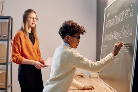 Selective focus shide view shot of African American boy writing music notes on blackboard during solfeggio lessonの写真素材