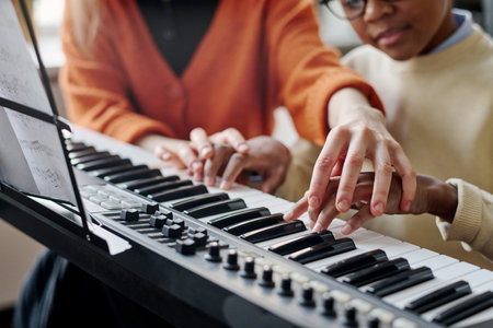 Selective focus shot of unrecognizable woman teaching Black boy to play synthesizer at music classの写真素材