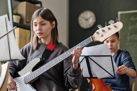 Selective focus shot of Caucasian teen girl practicing bass guitar during music lesson at school