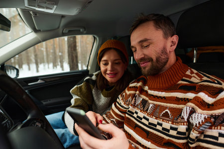 Cheerful Caucasian couple sitting in car reading map on smartphone