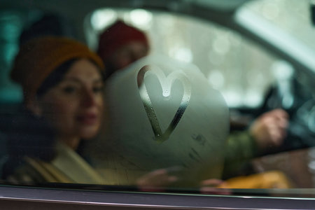 Selective focus shot of modern couple travelling by car looking at heart drawn on frosty windowの写真素材