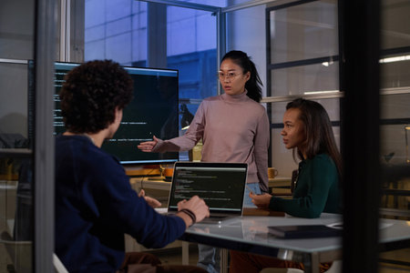 Ethnically diverse programmers working together on code at workplace in IT company office late in...