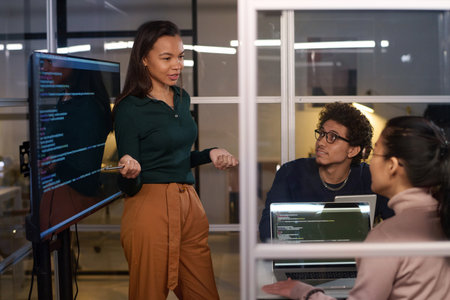 Ethnically diverse programmers working together on code at workplace in IT company office late in...
