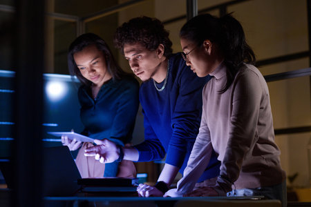 Group of modern young IT specialists developing and testing new software late in eveningの写真素材