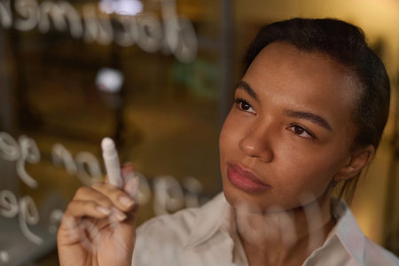 Young Black Woman developing code writing it on glass wallの写真素材