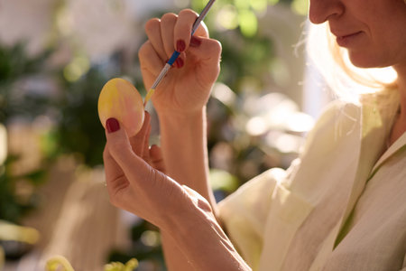 Closeup of Caucasian woman coloring egg for Easter holiday using brush and yellow paint