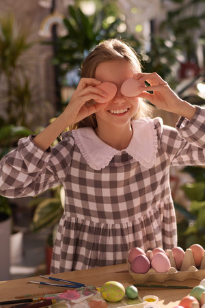 Vertical medium portrait of joyful Caucasian girl having fun posing for camera with Easter eggs on eyesの写真素材