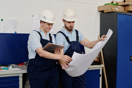 Medium long shot of male and female engineers working in factory checking technical drawing