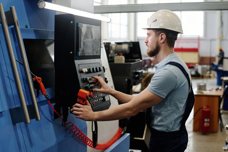Side view of young bearded Caucasian man wearing hardhat operating modern CNC machineの写真素材
