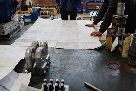 Group of three unrecognizable engineers working in factory looking through technical drawingsの写真素材