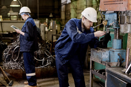 Man and woman wearing uniform working in industrial workshop using digital tablet and old-fashioned equipmentの写真素材
