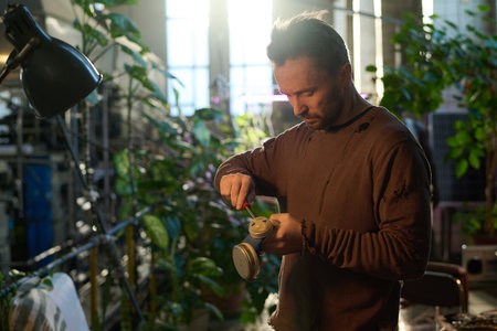 Medium shot of Caucasian man wearing distressed sweatshirt repairing old air-purifying respirator,...