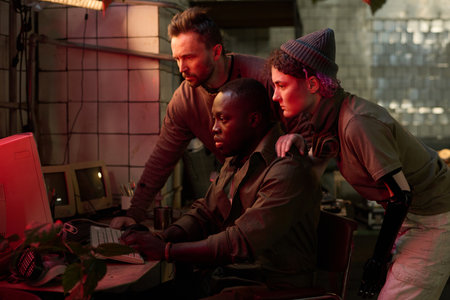 Group of three diverse people surviving apocalypse checking data on old computer in abandoned...