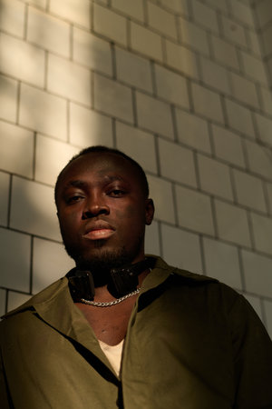 Vertical low angle view shot of young African American man wearing khaki green shirt and retro...