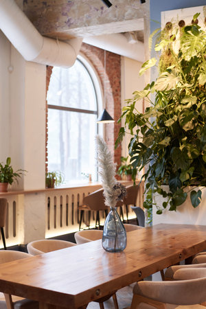 Vertical no people shot of part of modern restaurant interior with flowers in glass vase on wooden...