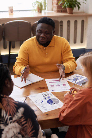 Vertical high angle over-the-shoulder of young Black man and two diverse women wearing casual...