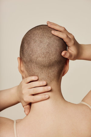 Rear view studio shot of unrecognizable woman with extremely short hair touching her head and neckの写真素材