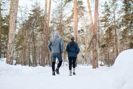 Wide rear view shot of unrecognizable senior man and woman in sportswear walking along forest park on winter dayの写真素材