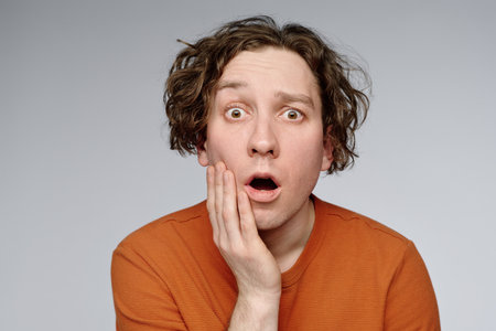 Medium closeup studio portrait of young Caucasian man with wavy hair looking at camera showing surprise emotion, copy spaceの写真素材