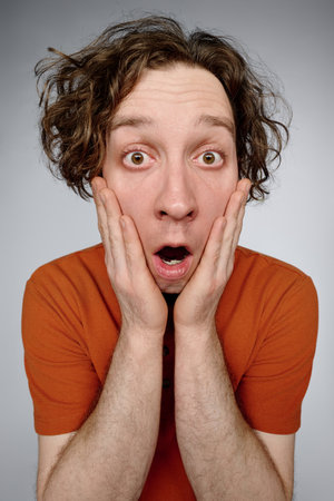 Vertical medium studio closeup of young Caucasian man with curly hair showing facial expression of astonishmentの写真素材