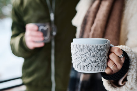 Closeup shot of unrecognizable man and woman holding mugs with hot tea or coffee standing outdoors on winter dayの写真素材