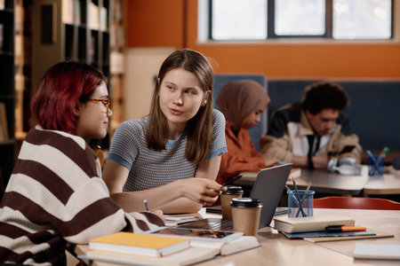 Young Caucasian and Asian girls sitting at table in university library doing homework or preparing for testsの写真素材