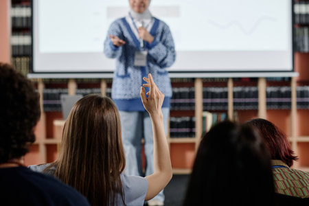 Selective focus shot of unrecognizable female student raising hand during lecture or conference in...