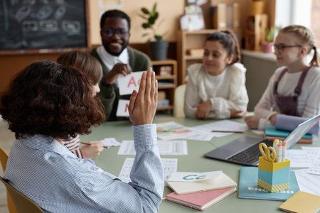 Unrecognizable Black boy attending language class sitting at table raising hand to ask questionの写真素材