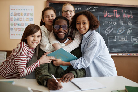 Group portrait of ethnically diverse students standing in classroom hugging their teacher and smiling at camera, copy spaceの写真素材