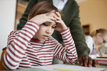 Medium closeup of Caucasian boy sitting at table in class struggling to do difficult task,...
