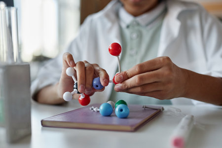 Closeup of hands of unrecognizable Black schoolboy wearing white lab coat sitting at desk assembling molecular structure modelの写真素材