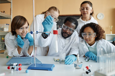 Young African American teacher of Chemistry sitting at table in classroom demonstrating lab experiment to group of kidsの写真素材