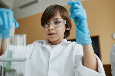 Medium closeup of Caucasian boy wearing lab coat and goggles working on experiment during Chemistry lesson at schoolの写真素材