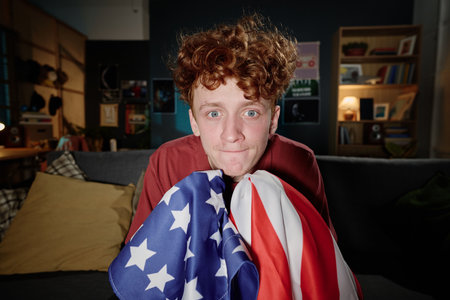 Medium closeup of Caucasian guy holding flag sitting in living room watching sports event on TVの写真素材