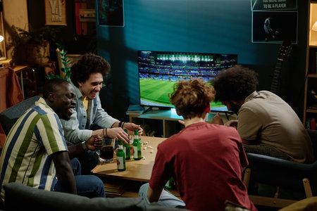 Young ethnically diverse friends enjoying spending evening together watching soccer game, drinking...