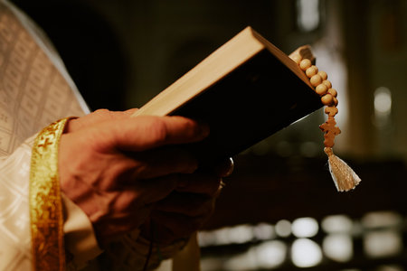 Closeup of hands of unrecognizable Catholic priest holding Bible book with rosary