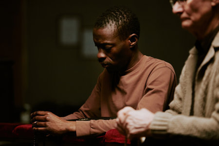 Selective focus shot of senior Caucasian and young Black men holding rosary praying during service in Catholic churchの写真素材