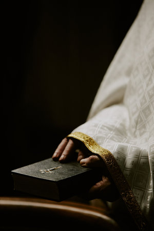 Vertical closeup low key of hands of unrecognizable elderly Catholic pastor taking Holy Bible or prayer bookの写真素材