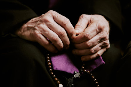 Closeup of wrinkled hands of unrecognizable elderly Catholic priest holding rosaryの写真素材