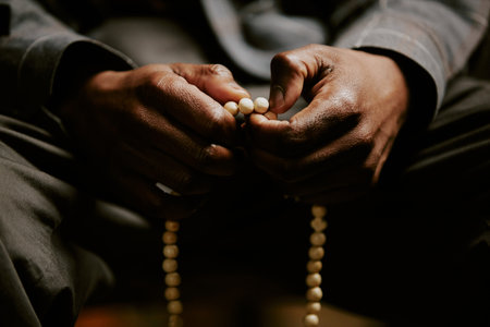 Closeup shot of unrecognizable African American male parishioner praying with rosary in handsの写真素材