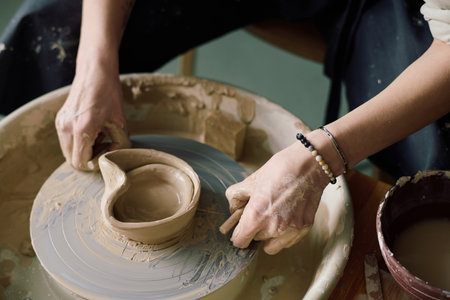 High angle closeup of hands of unrecognizable woman shaping modern vessel on potters wheel in...