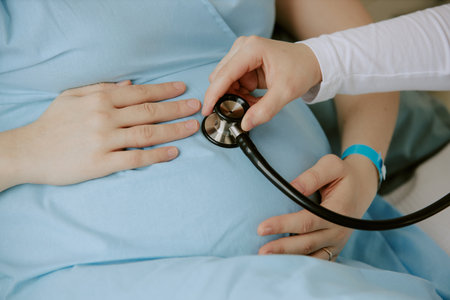 Medium close up of pregnant woman holding her belly while obstetrician checking heartbeat of fetusの写真素材