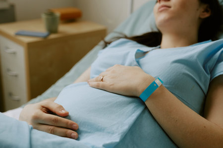 Pregnant patient lying on bed and caressing her tummy while she having contractionの写真素材