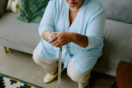 High angle photo of waiting mature African American female woman sitting on coach and holding caneの写真素材
