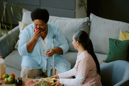 Mature patient inhaling fresh and sweet apple scent while young nurse dressed in scrubs sitting next...
